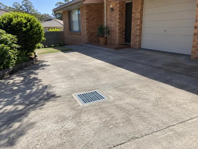 Clean outdoor drain grate set in a concrete driveway beside a brick house in Baulkham Hills