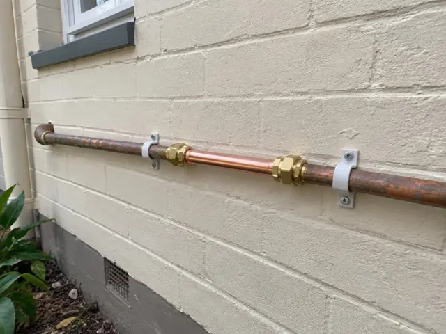 Exterior wall with a repaired copper water pipe section on a painted brick wall in Westmead